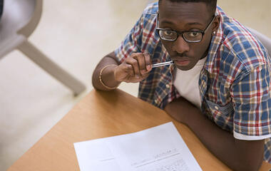 Portrait of male student wearing glasses sitting at desk in classroom